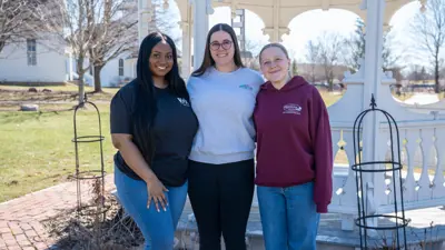 Group photo of the Meridian Township Communications Department that shows three staff members standing in the Meridian Historical Village